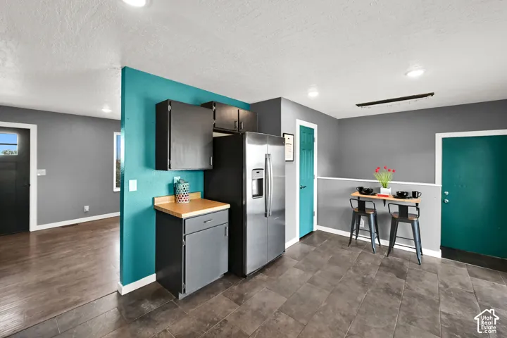 Kitchen area featuring dark tile flooring, stainless steel refrigerator, and dark cabinetry with a wood-finish countertop