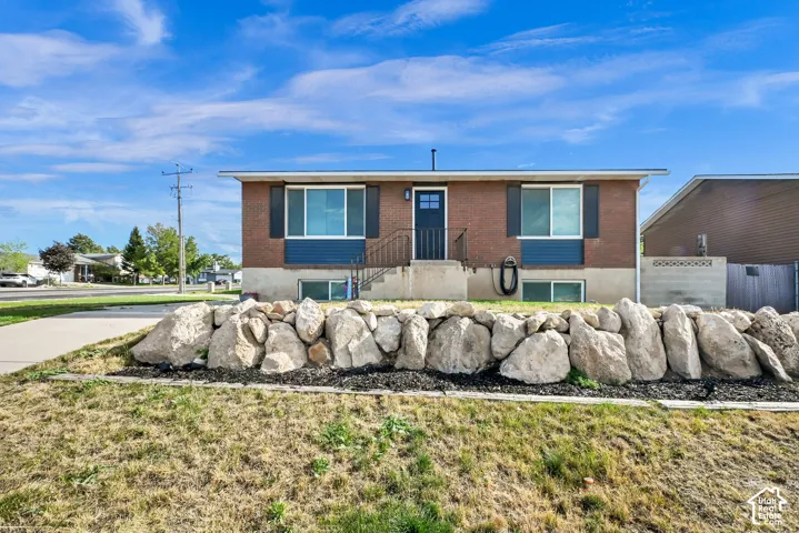 Brick and siding exterior with dark shutters, front entry door with side light, and an integrated rock retaining wall