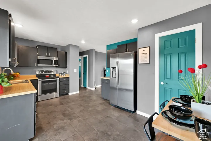 Modern kitchen featuring stainless steel appliances, dark cabinetry, wood-finish countertops, recessed lighting, and tile flooring