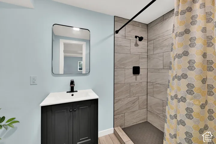 Bathroom featuring a black vanity with integrated sink, a rectangular framed mirror, matte black faucet, and a shower with full-height tile surround and a tiled floor
