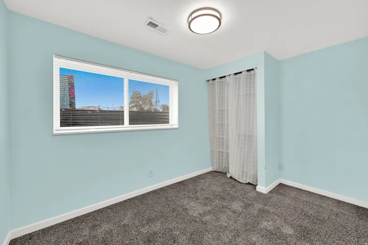 Room with textured carpet, light blue walls, a rectangular window with horizontal blinds, and a flush-mount ceiling light fixture