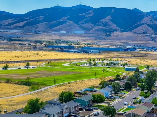Residential neighborhood with paved streets, surrounded by green spaces and distant mountains