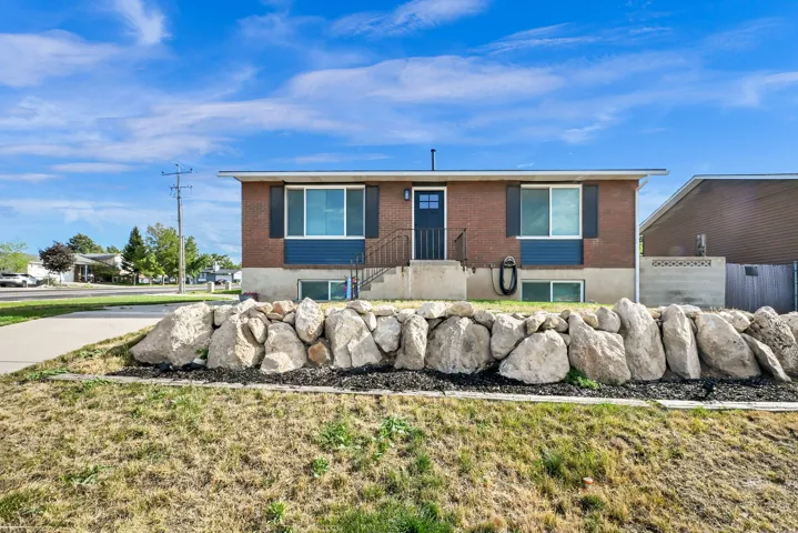 Brick and siding exterior with dark shutters, front entry door with side light, and an integrated rock retaining wall