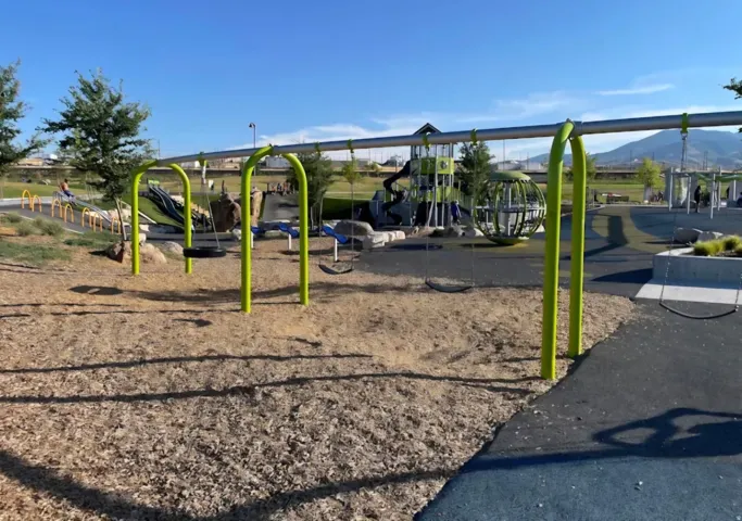 Community playground with multiple swing sets, a slide, climbing structures, and a wood chip ground cover