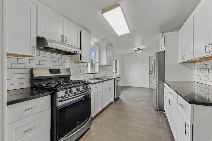 White cabinetry with brushed nickel hardware, dark countertops, white subway tile backsplash, stainless steel range with hood, and wood-finish flooring