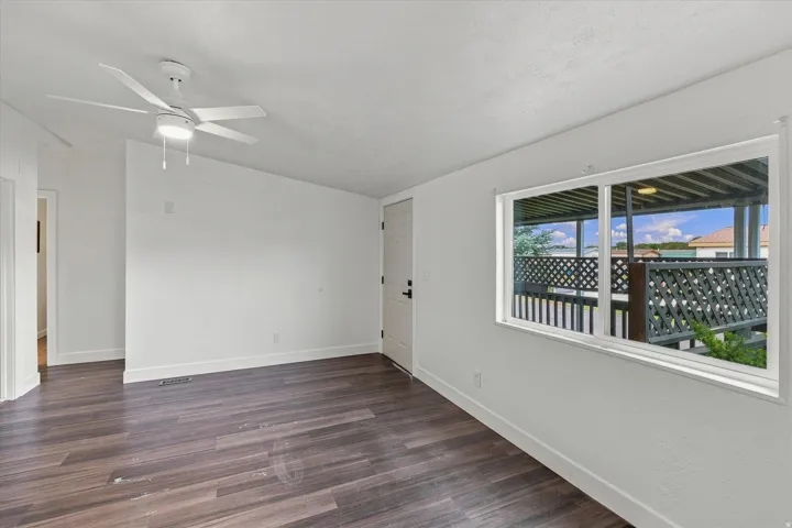 Spacious room showcasing rich wood-finish flooring, neutral painted walls, and a ceiling fan with integrated lighting
