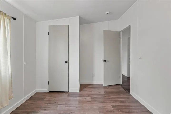 Bright hallway showcasing warm wood-finish flooring, multiple white panel doors with black hardware, and clean white walls with recessed ceiling lighting