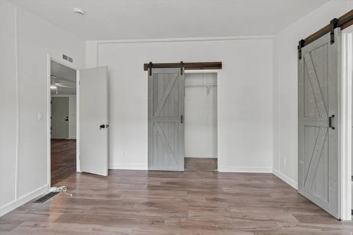 Wood-finish flooring, two sliding barn doors, white walls, and a closet with carpeting and shelving