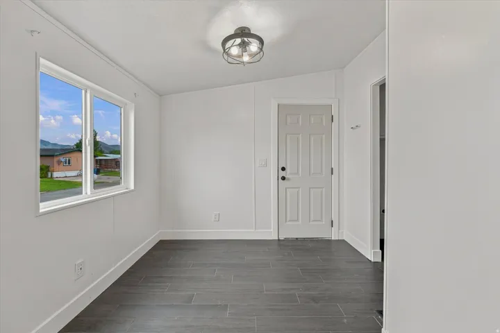 White paneled walls, dark tile flooring, interior door with black hardware, and an overhead semi-flush mount light fixture