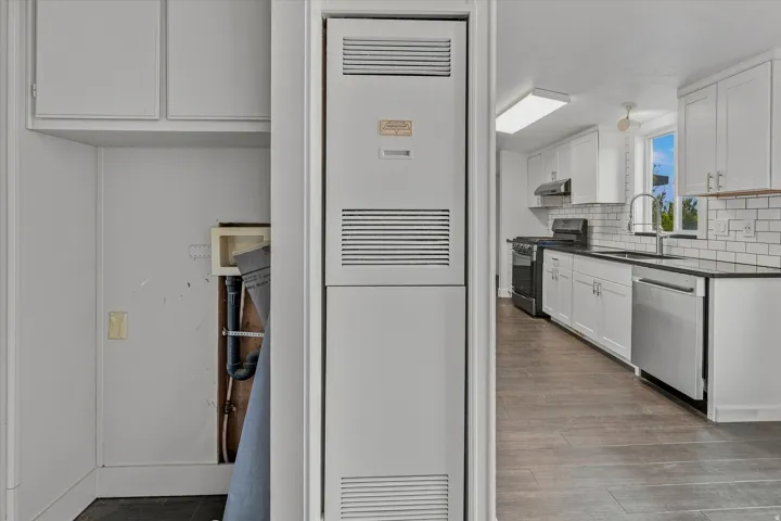 Efficient galley kitchen with white cabinetry, stainless steel appliances, subway tile backsplash, and wood-finish flooring