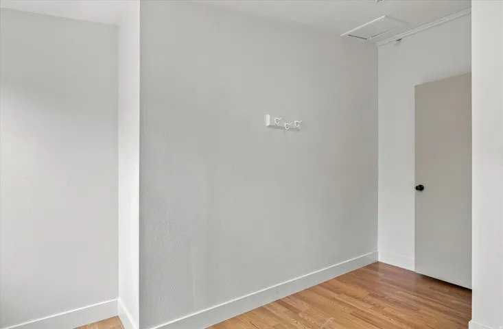 Wood-finish flooring with white baseboards, white textured walls, and a white interior door with a black knob