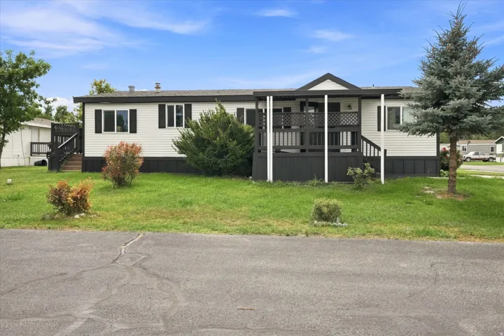 White siding exterior with black trim, covered front porch, front deck, established landscaping, and mature tree