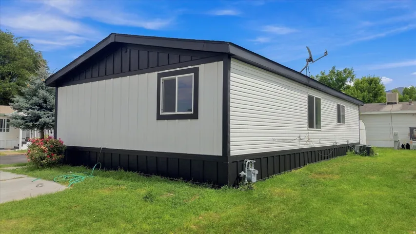 Modern manufactured home featuring a sleek black and white exterior with board-and-batten accents, multiple windows for natural light, and a spacious foundation with skirting