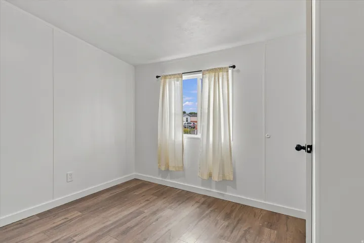 Wood-finish flooring, white panel walls, and a window with natural light