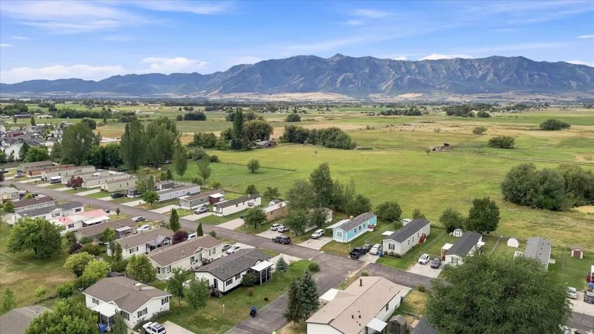 Aerial view showcasing a residential community nestled within expansive green valleys, with mature tree-lined properties, multiple single-family homes with varied architectural styles, and mountain ranges visible in the distance
