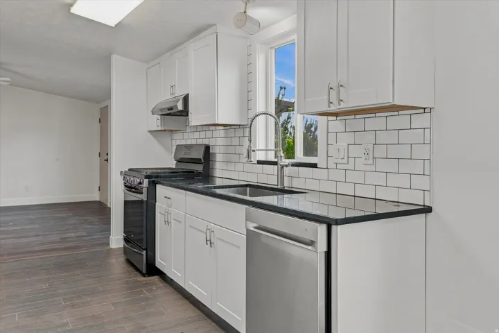 Kitchen featuring white cabinetry, dark countertops, a stainless steel sink with a gooseneck faucet, subway tile backsplash, and wood-finish flooring