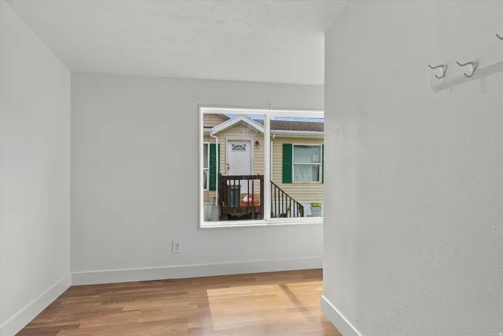 Wood-finish flooring with white baseboards, bright white walls, and a white window frame with clear glass