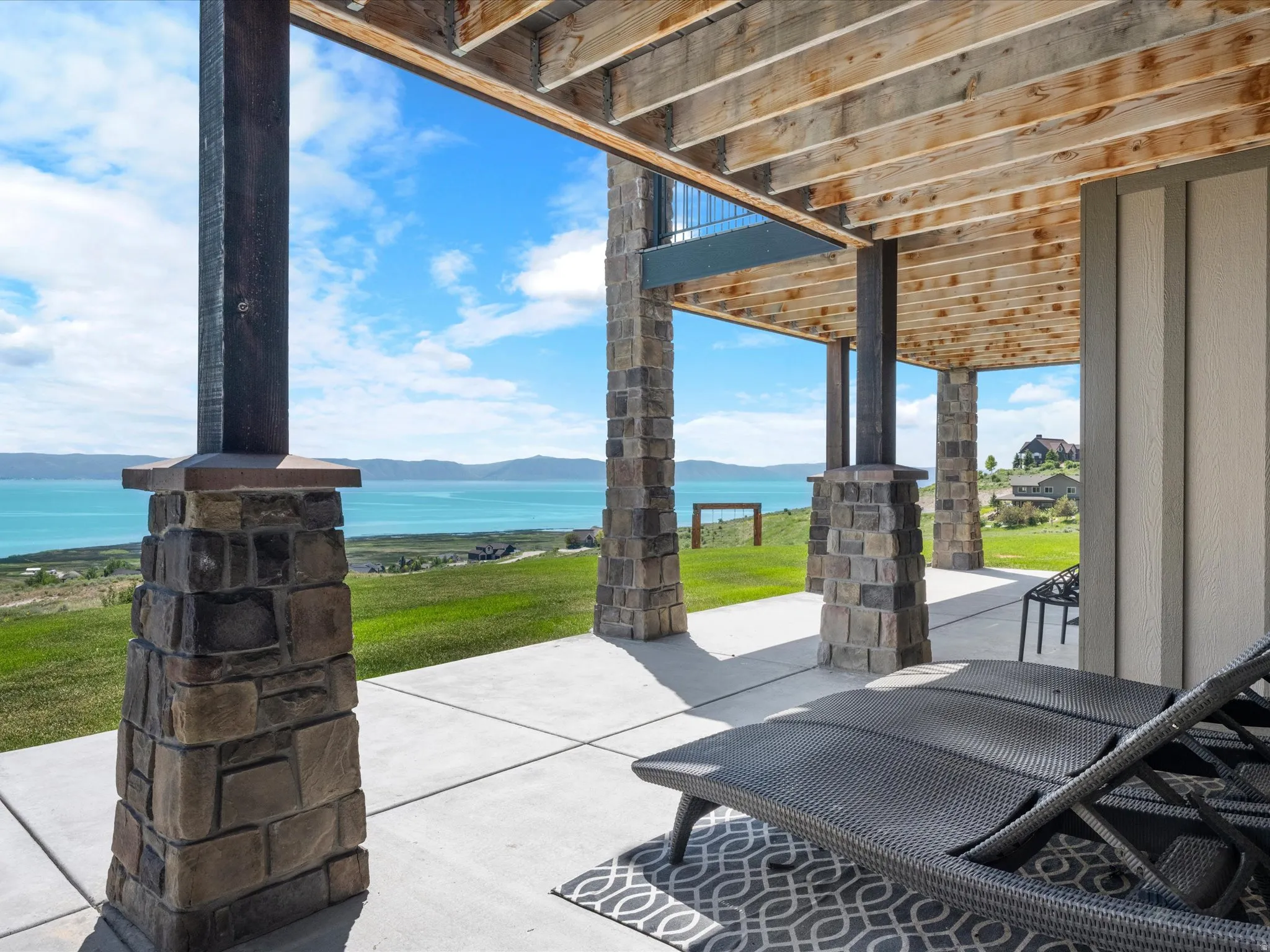 Covered patio with concrete flooring, stone-wrapped columns, and exposed wood beam ceiling