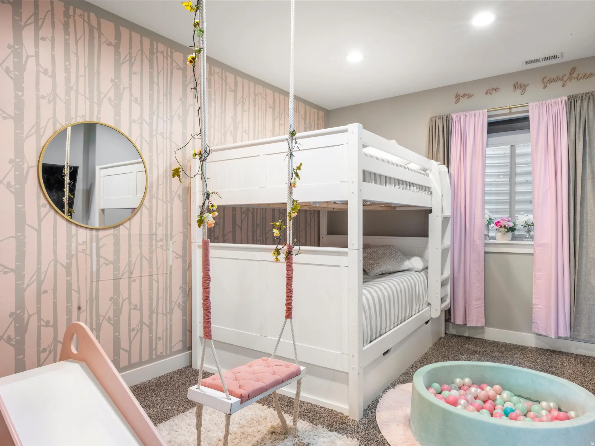 Recessed ceiling lighting, gray wall paint, window with pink and gray drapery, and wall-mounted round gold-finish mirror