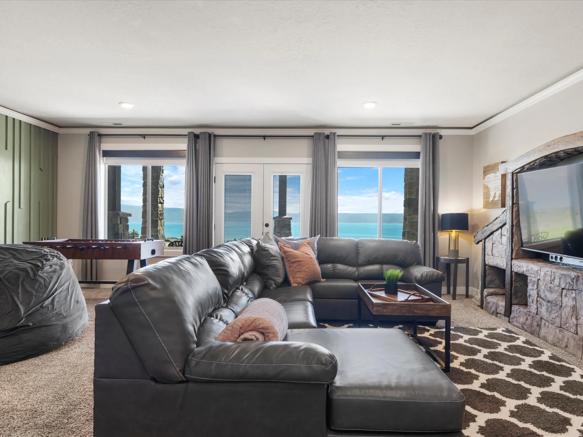 Stone-clad media console, recessed lighting, expansive windows, glass-paneled French doors, and textured accent wall