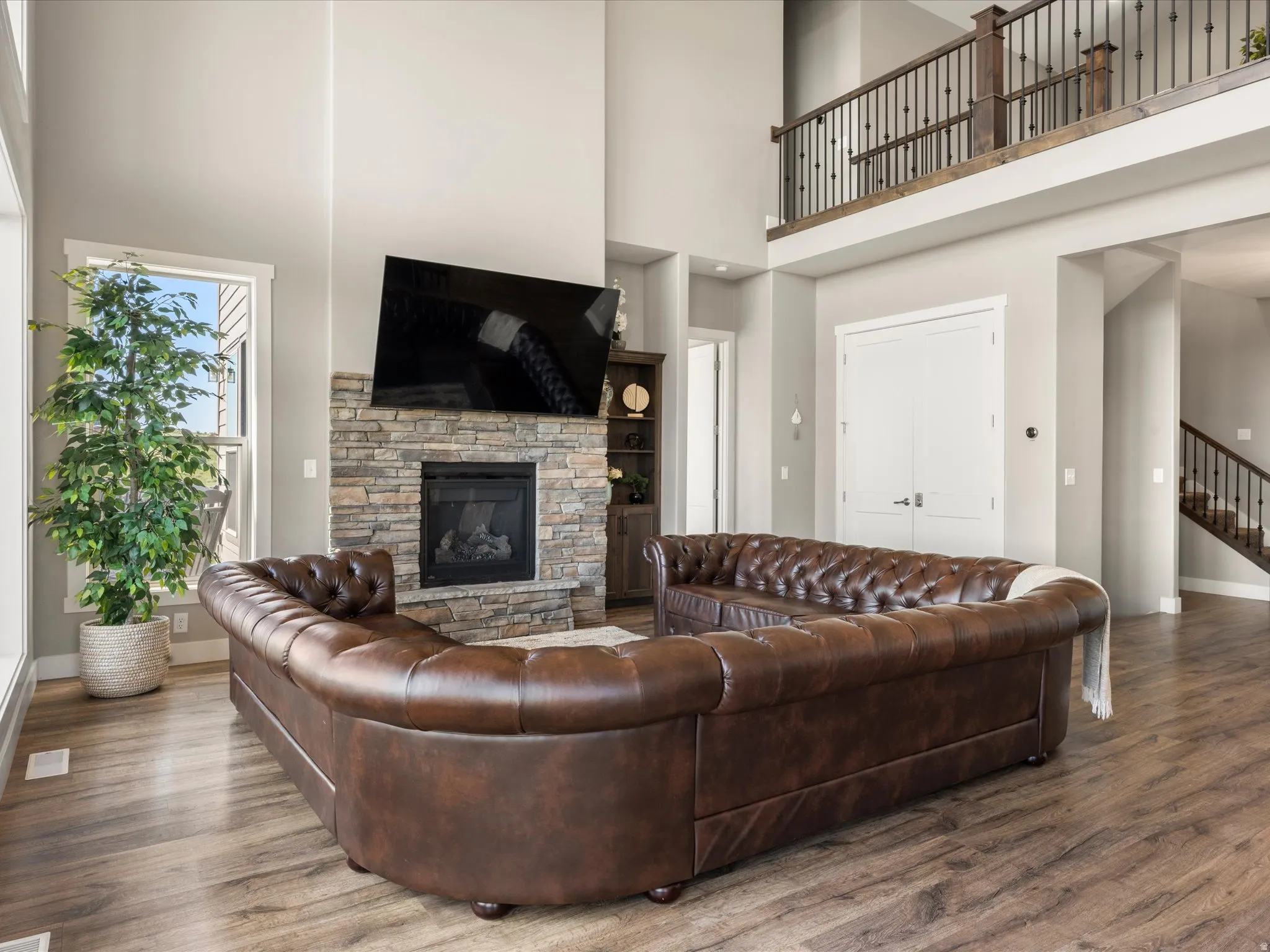 Two-story living area featuring wood-finish flooring, a stone-clad fireplace, and an open balcony with metal balusters
