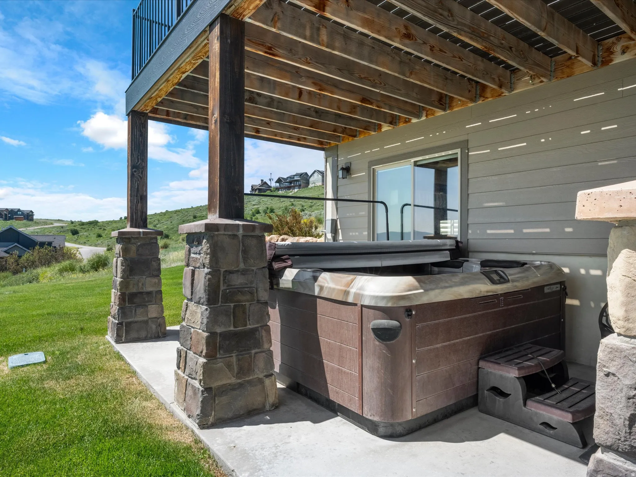 Covered patio with an integrated spa, stone-clad support columns, and sliding glass door access