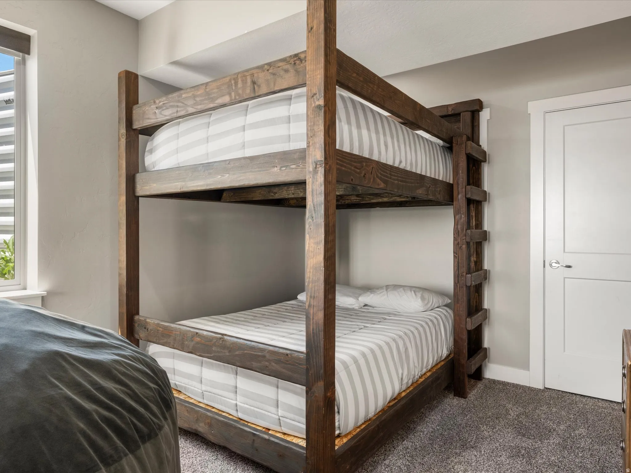 Built-in wooden bunk beds with a ladder, featuring neutral wall paint and carpeted flooring