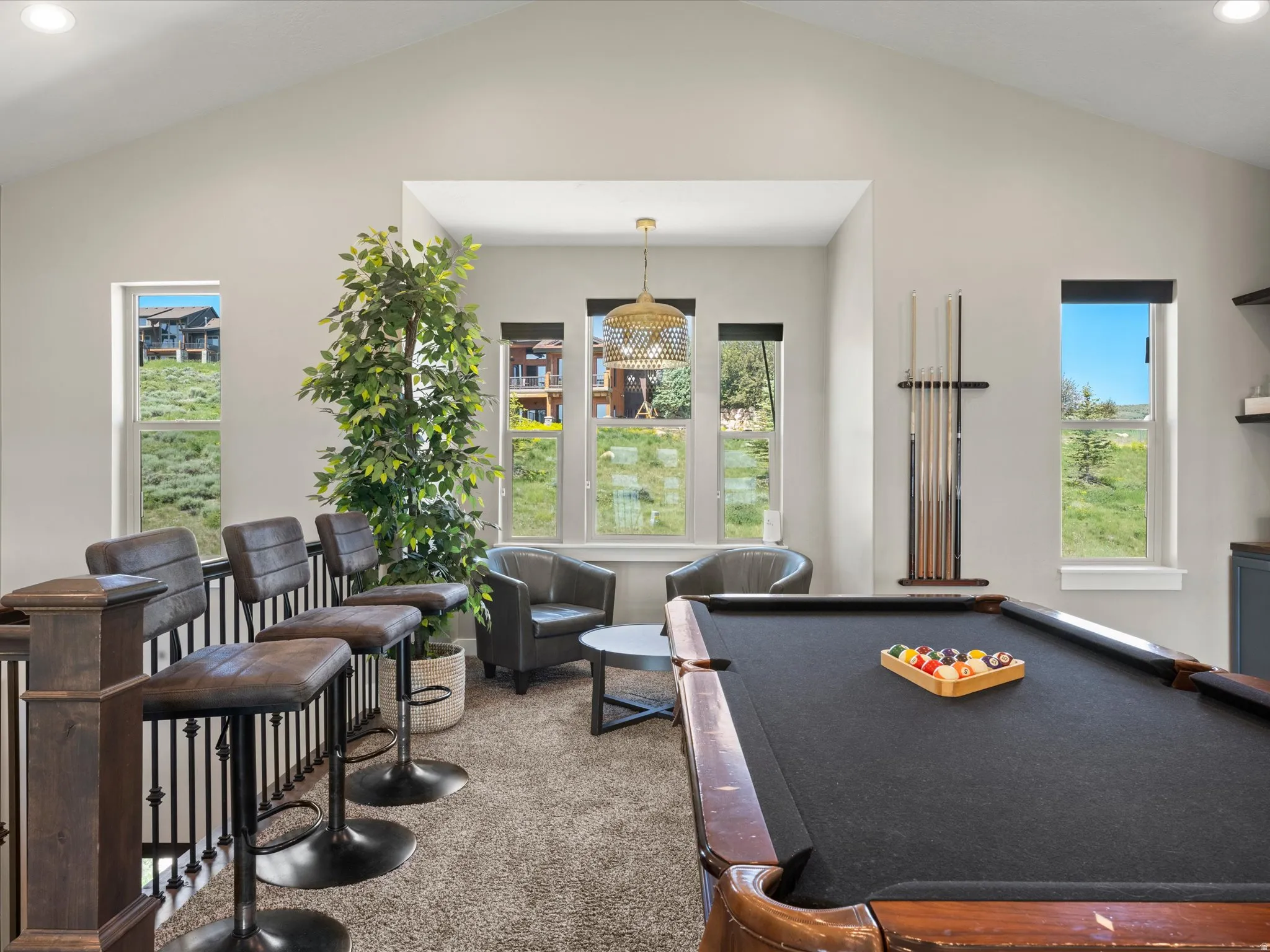 Recreation room featuring a pool table with wood-finish frame and black playing surface, abundant natural light from multiple French doors and windows, neutral carpeting, built-in cabinetry along the perimeter, and a brass pendant light fixture suspended