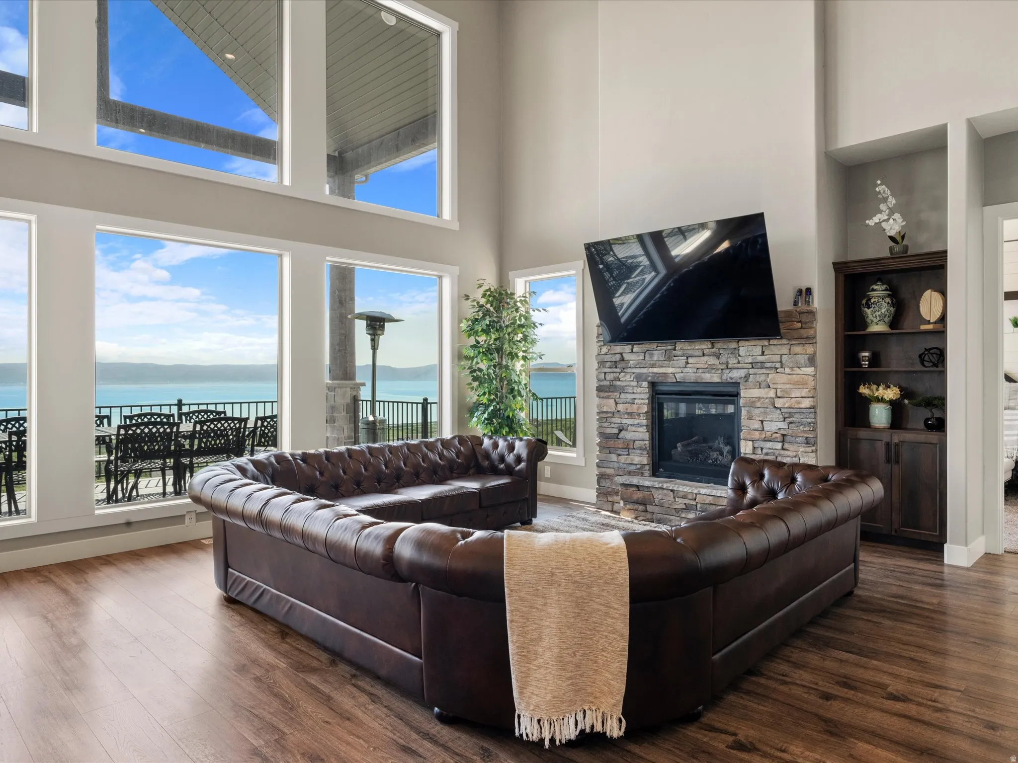Great room featuring soaring ceilings, a stone fireplace, wood-finish flooring, built-in cabinetry, and expansive window walls
