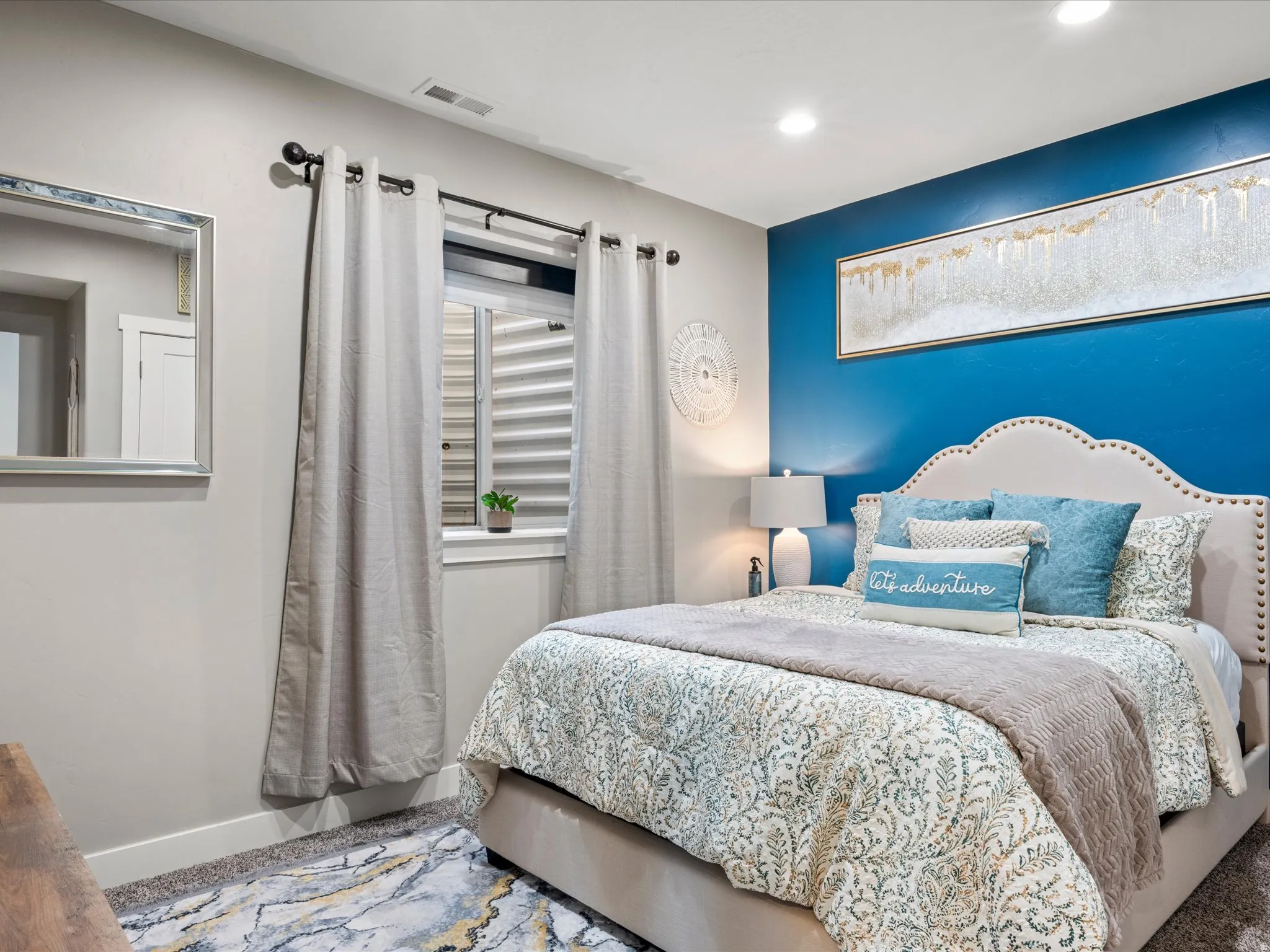 Recessed lighting, window with horizontal blinds, wall-mounted mirror, and a feature wall with a contrasting paint finish