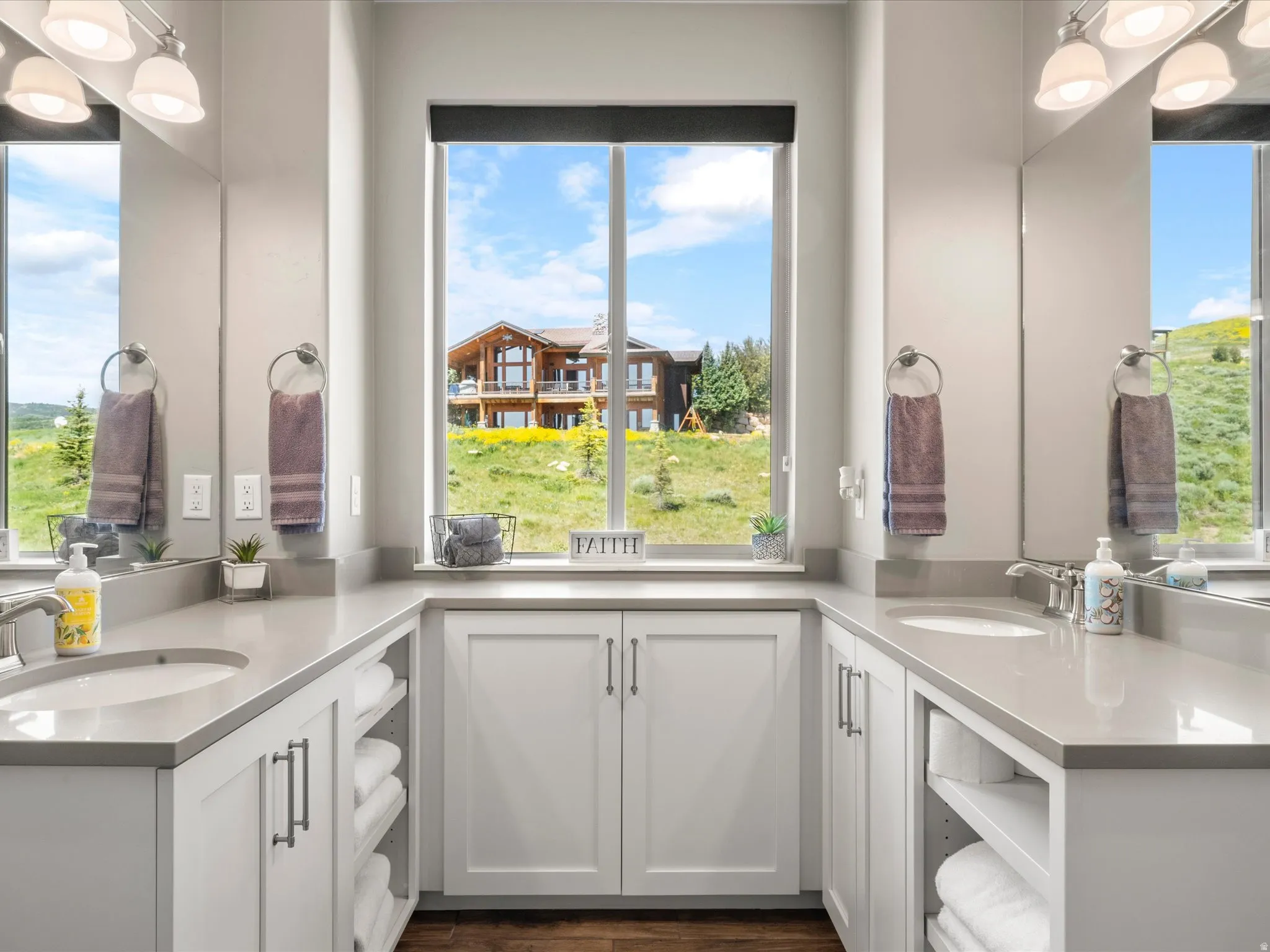 Dual vanities with undermount sinks, expansive countertop space, white cabinetry with storage, and a large central window