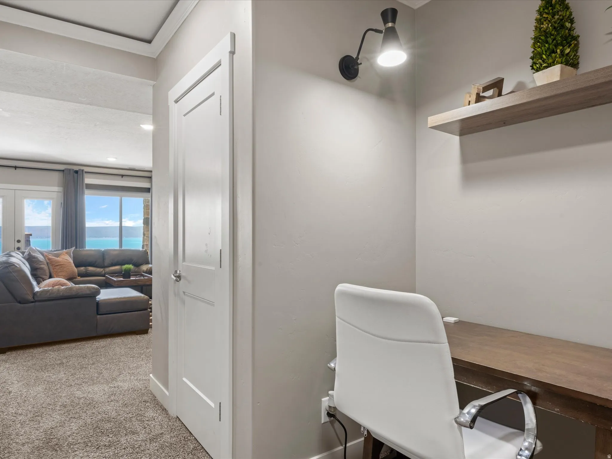 Dedicated desk alcove featuring a wall-mounted sconce, integrated desk surface, and a floating wood-finish shelf
