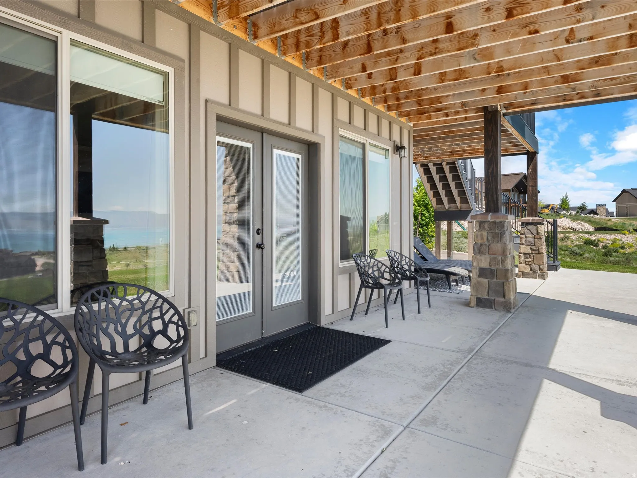 Concrete patio featuring board-and-batten siding, large windows, double doors, and stone-clad columns
