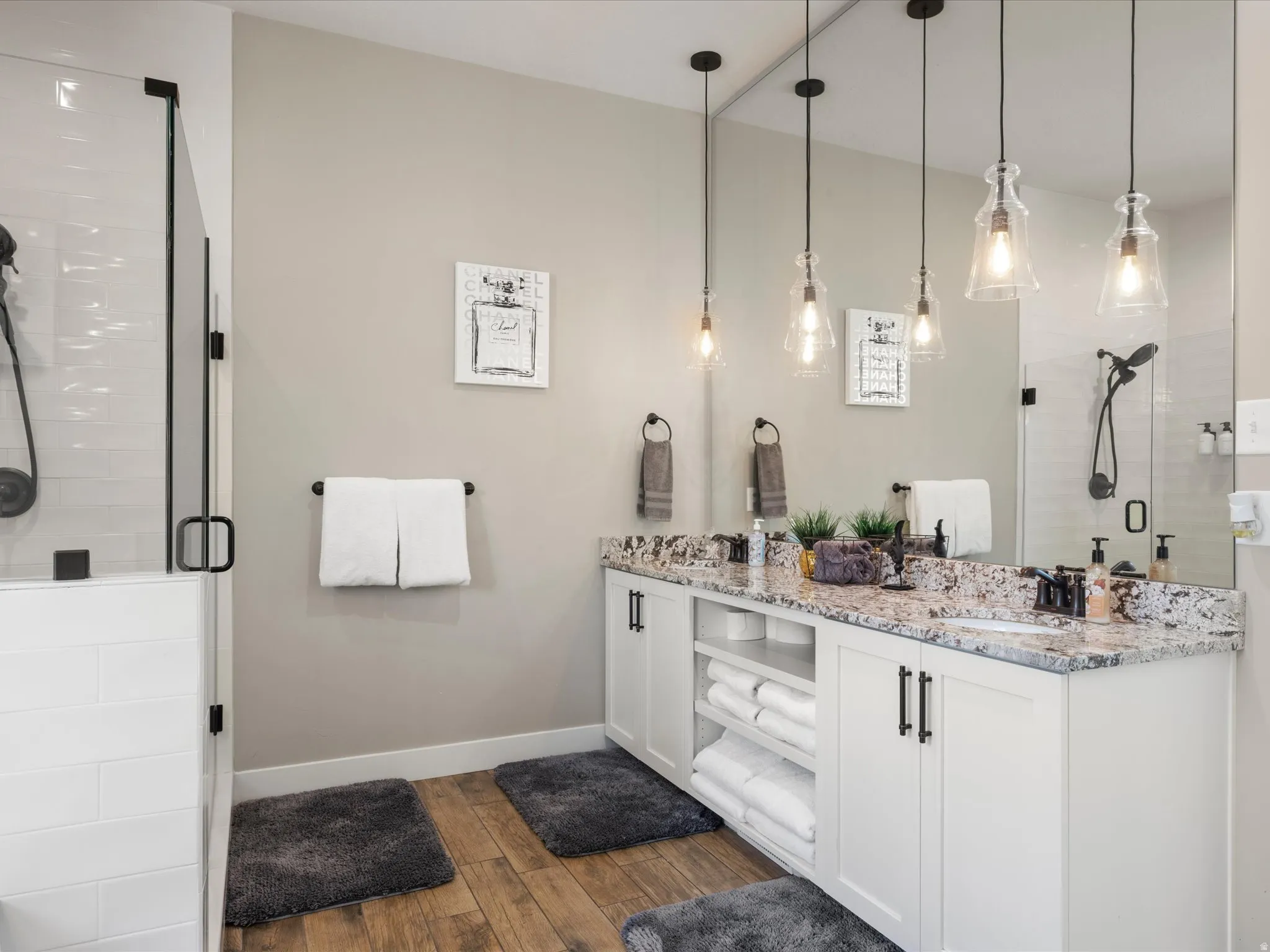 Dual vanity with granite countertops, wood-finish flooring, and pendant lighting