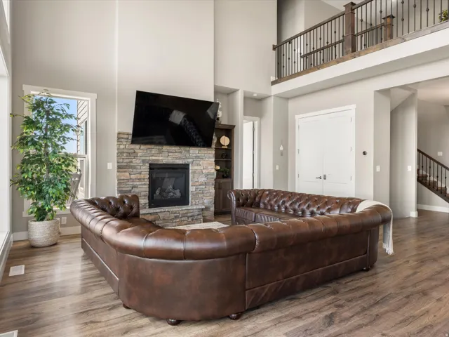 Two-story living area featuring wood-finish flooring, a stone-clad fireplace, and an open balcony with metal balusters