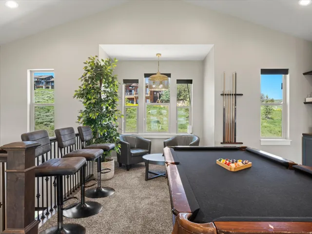 Recreation room featuring a pool table with wood-finish frame and black playing surface, abundant natural light from multiple French doors and windows, neutral carpeting, built-in cabinetry along the perimeter, and a brass pendant light fixture suspended