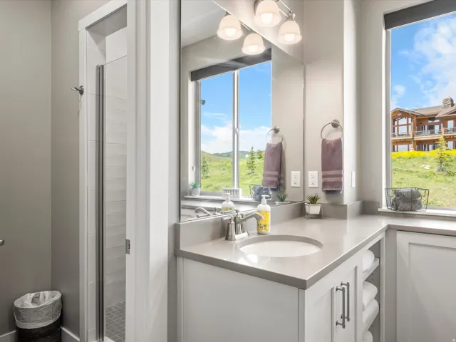 Walk-in shower with glass enclosure, single vanity with integrated sink, stone countertop, built-in storage shelving, and large windows