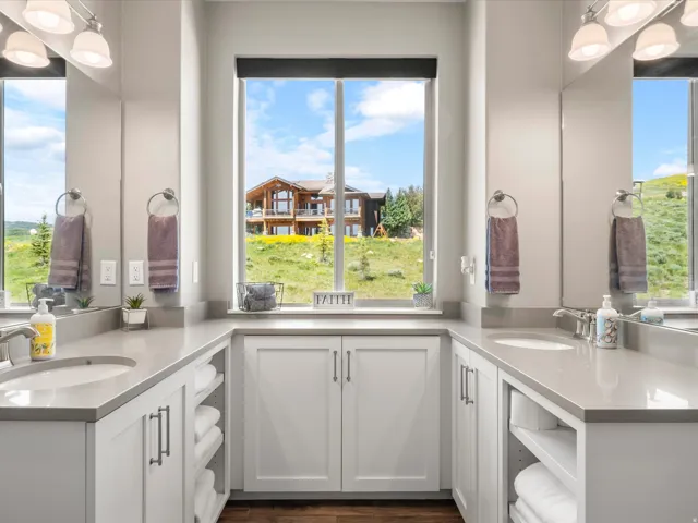 Dual vanities with undermount sinks, expansive countertop space, white cabinetry with storage, and a large central window