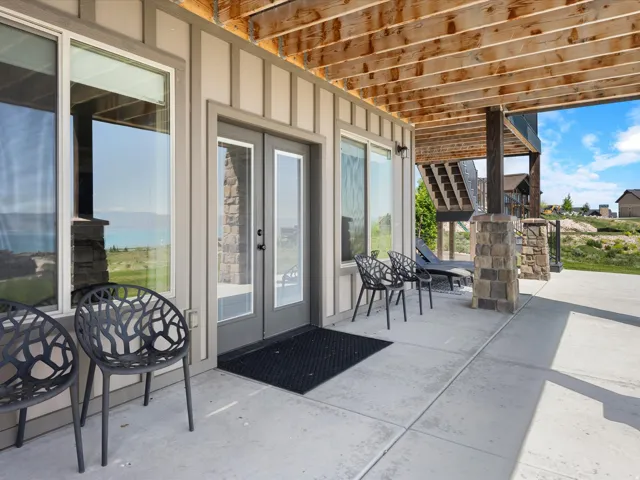 Concrete patio featuring board-and-batten siding, large windows, double doors, and stone-clad columns
