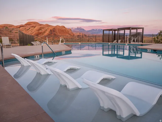 Resort-style pool featuring submerged lounge seating, dual pergolas, and a surrounding deck