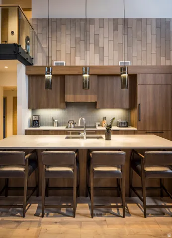 Modern kitchen featuring a large island with integrated sink, wood-finish cabinetry, a tiled backsplash, and recessed lighting