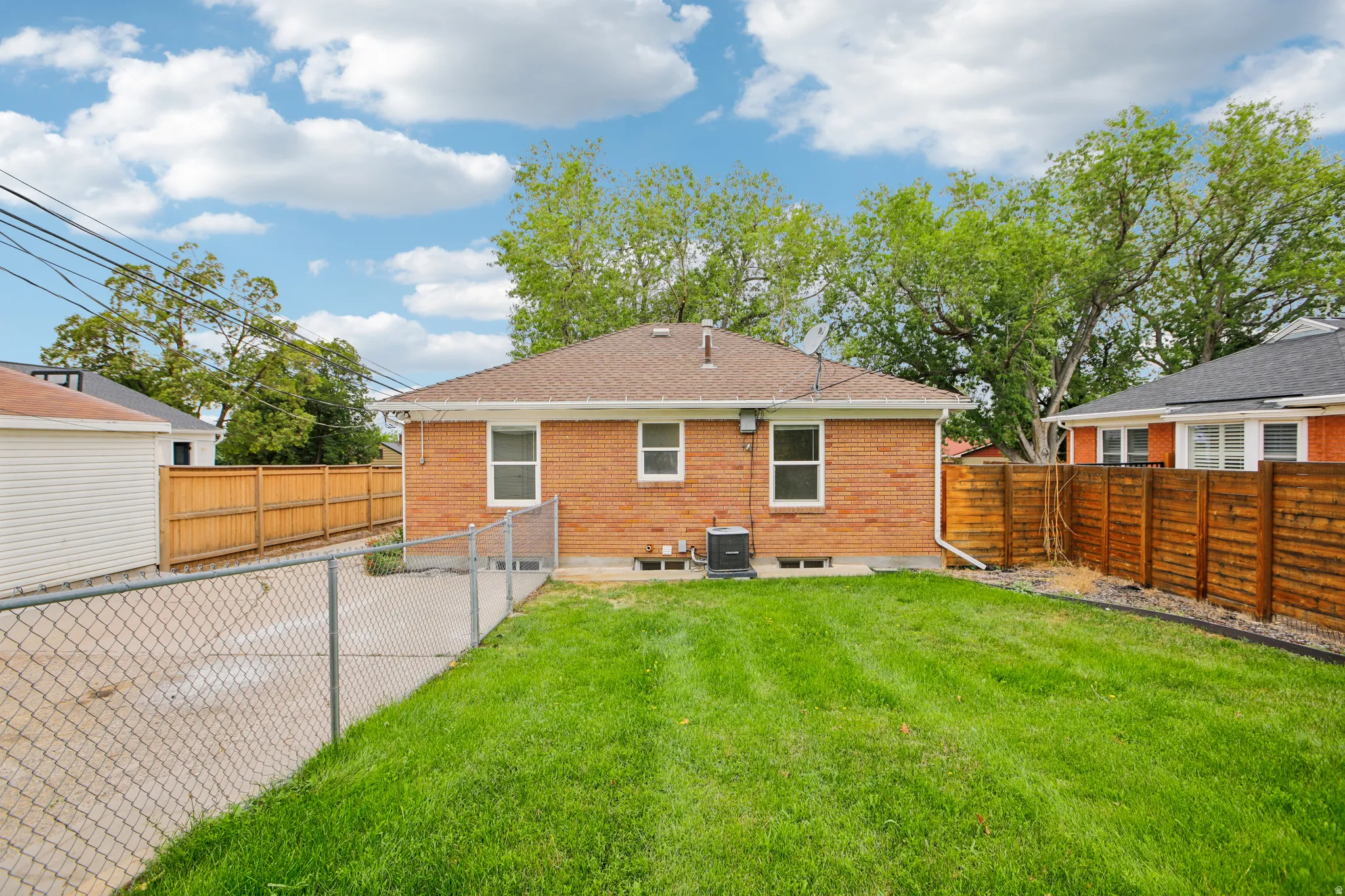 Expansive green lawn with a chain link fence, brick exterior with white trim windows, and a wood privacy fence