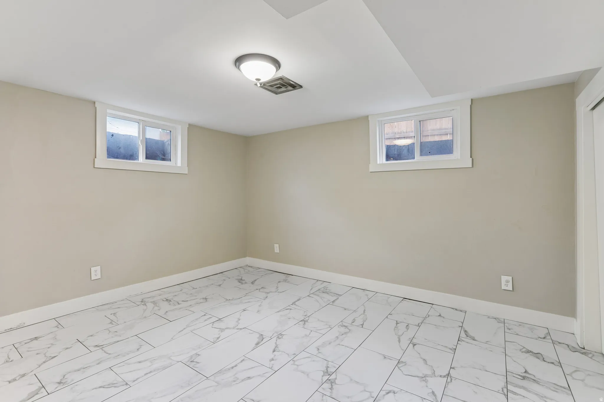 Recessed lighting with a flush-mount fixture, two framed windows, light-toned wall paint, and marble-patterned tile flooring