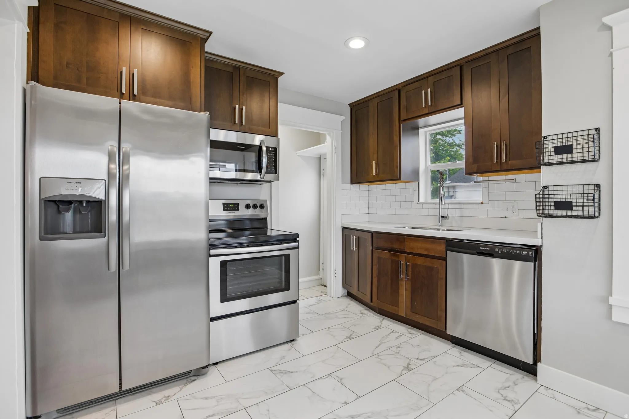 Dark wood-finish cabinetry, stainless steel appliances, white subway tile backsplash, white countertop, and patterned floor tiling