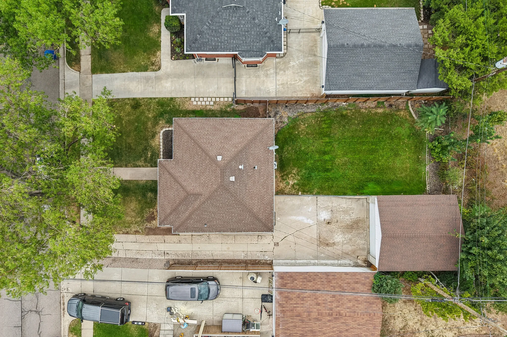 Expansive lot featuring a main residence with a brown shingle roof, a detached garage with a brown shingle roof, a large grassy backyard, and mature trees