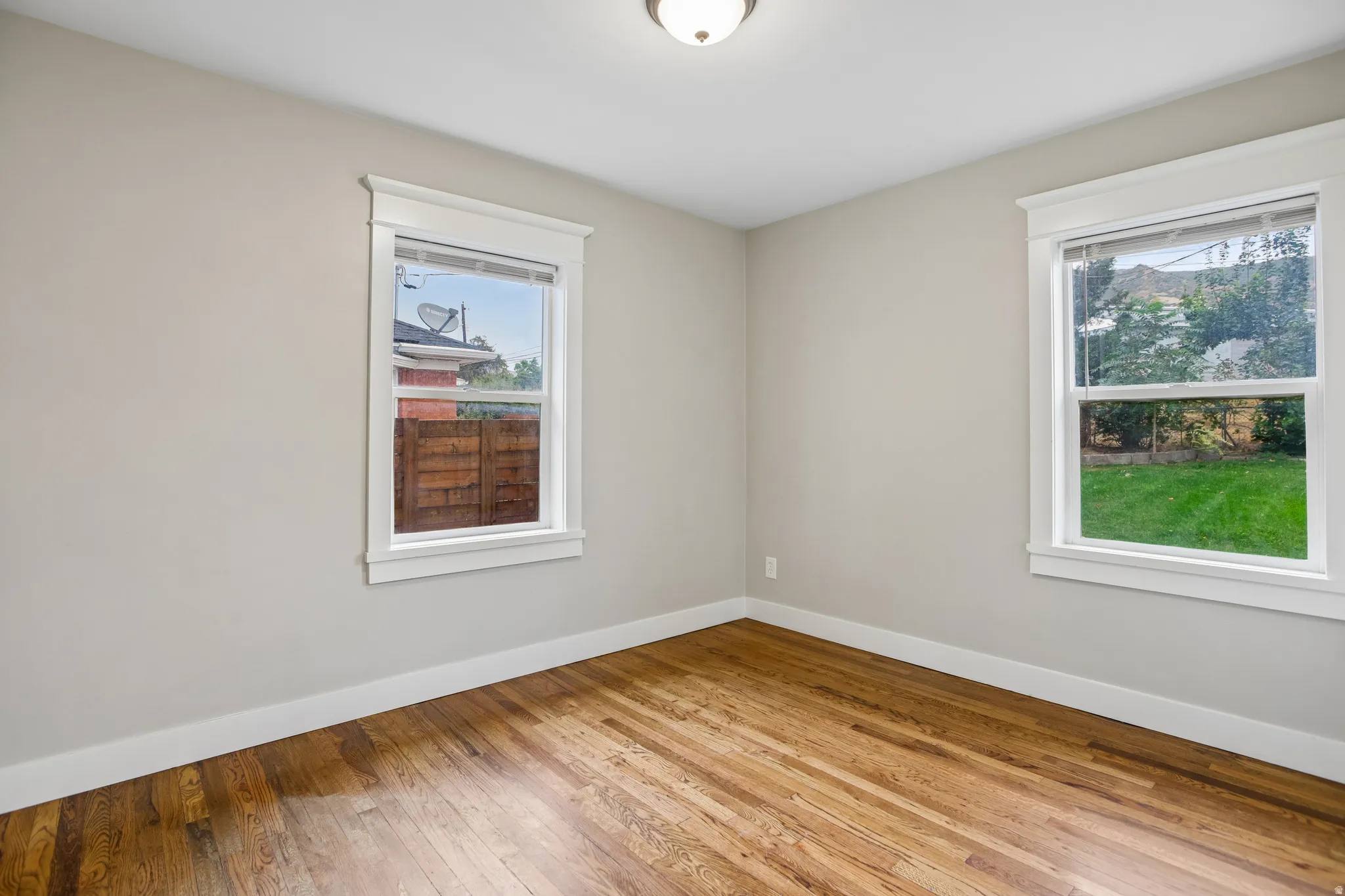 Hardwood flooring, neutral wall tones, white trim, dual windows, and ceiling-mounted lighting