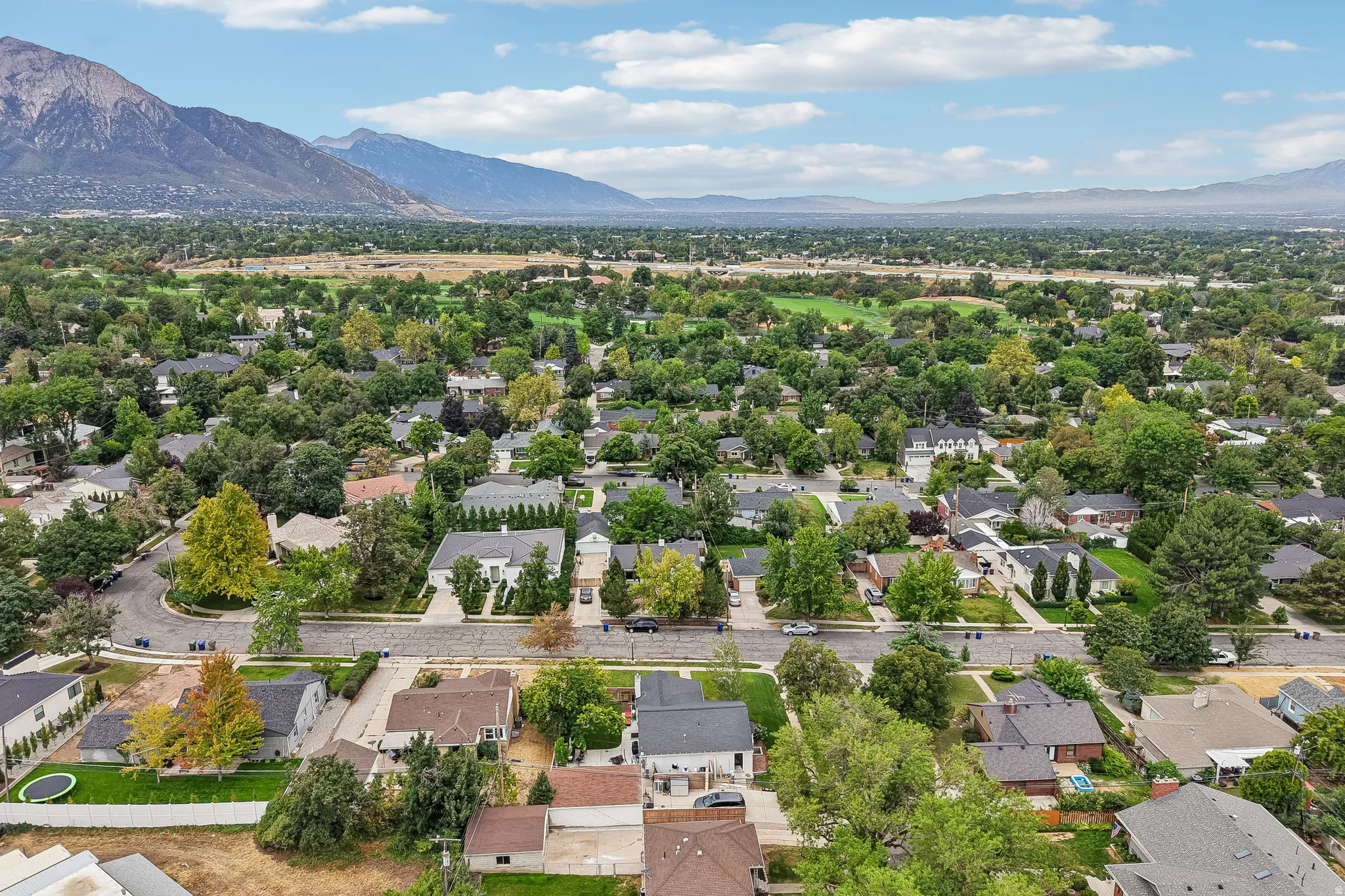 Expansive residential neighborhood with mature trees, mountain backdrop, and golf course in the distance