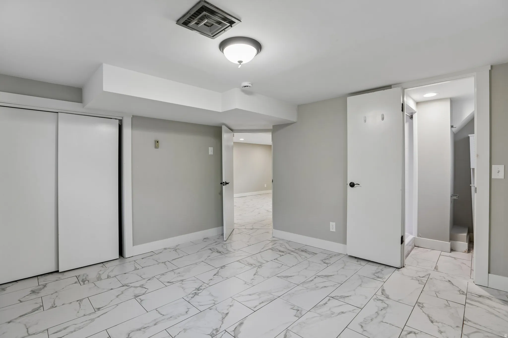 White marble-look tile flooring, light gray walls, white trim, sliding closet doors, and recessed ceiling lighting