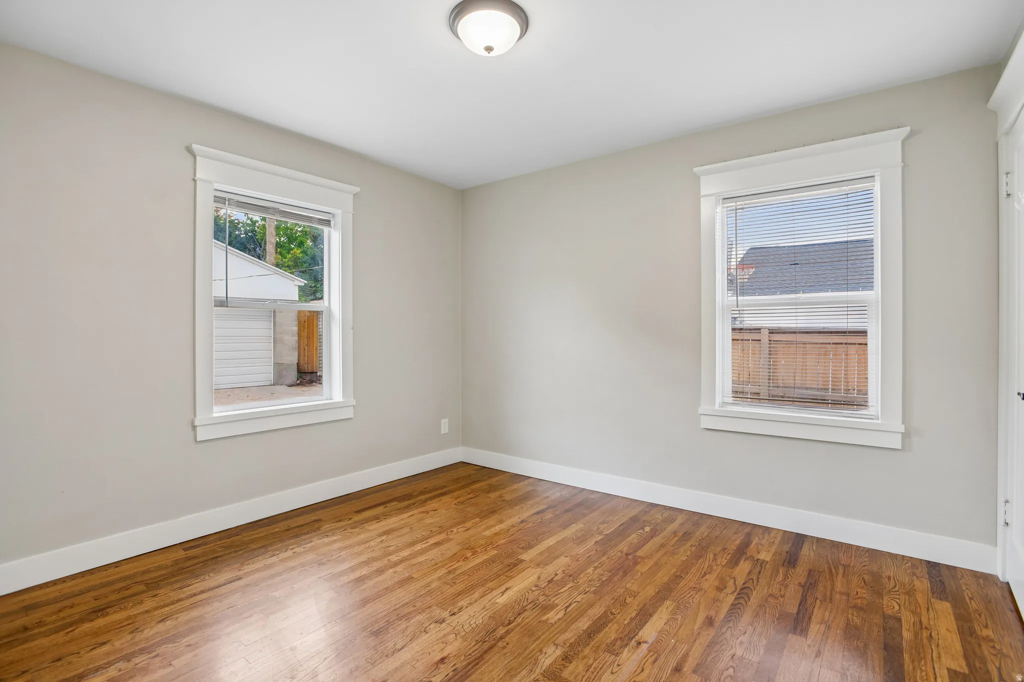 Wood-finish flooring, two windows with white trim, neutral wall tones, and a ceiling-mounted light fixture