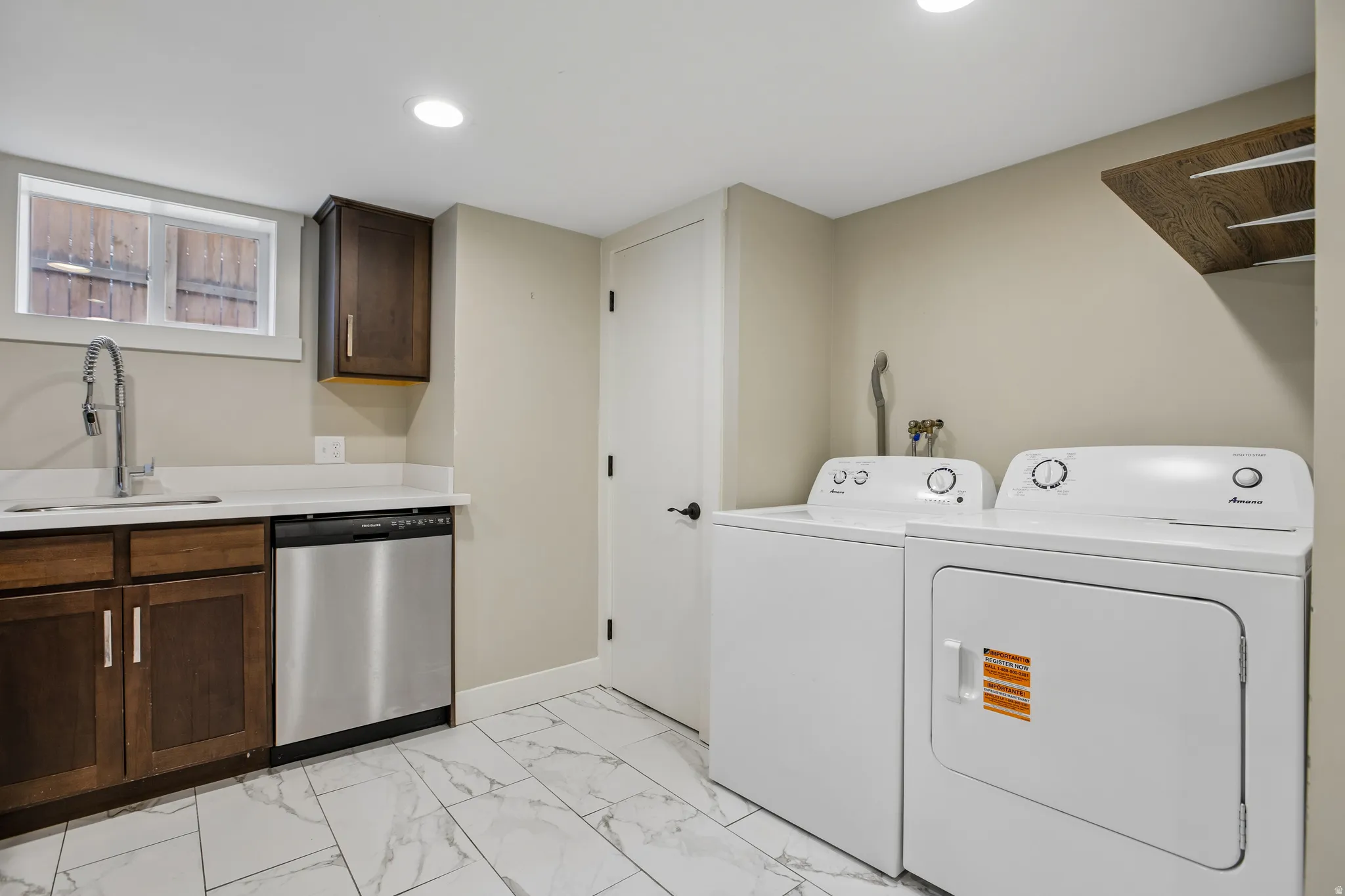Utility space featuring a stainless steel dishwasher, white countertops, dark wood cabinetry, a stainless steel sink with a gooseneck faucet, and white tile flooring